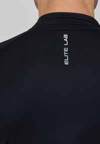 Schwarzes Sportshirt mit hohem Ausschnitt, das ein elegantes, eng anliegendes Design aufweist und ein weißes "ELITE LAB"-Logo hat, das vertikal auf dem Rücken platziert ist.