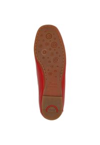 Semelle d'une chaussure en cuir rouge avec une semelle en caoutchouc marron dotée de crampons circulaires et le nom de la marque "Sioux" embossé près du talon.