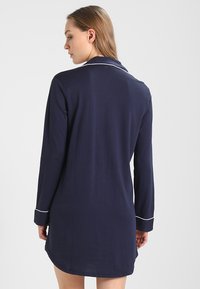 Mørkeblå nattkjole med lange ermer og avslappet passform, hvite kanter på kragen og mansjettene, mykt stoff og lengde midt på låret.