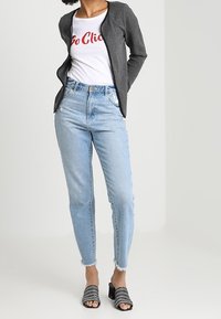 Ljust grå strukturblazer över en vit t-shirt med röd text, matchad med ljusblå jeans och svarta klackskor.