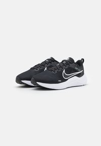 Crne atletske tenisice s teksturiranim mrežastim gornjim dijelom, bijelim potplatom i istaknutim bijelim Nike logom sa strane. Imaju dizajn s vezicama.