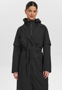 Svart vattentät trenchcoat med huood, med bälte i midjan, långa ärmar och tryckknappsstängning. Slät textur och minimalistisk design.