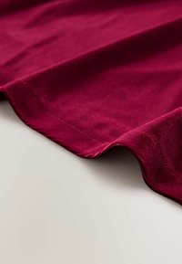 Bordeaux stof met een zachte textuur en een gladde afwerking, voorzien van een strakke zoom en subtiele stikdetails langs de randen.