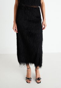 Black fringe two-piece outfit featuring a cropped top and skirt, paired with black sandals adorned with white beads and bows.
