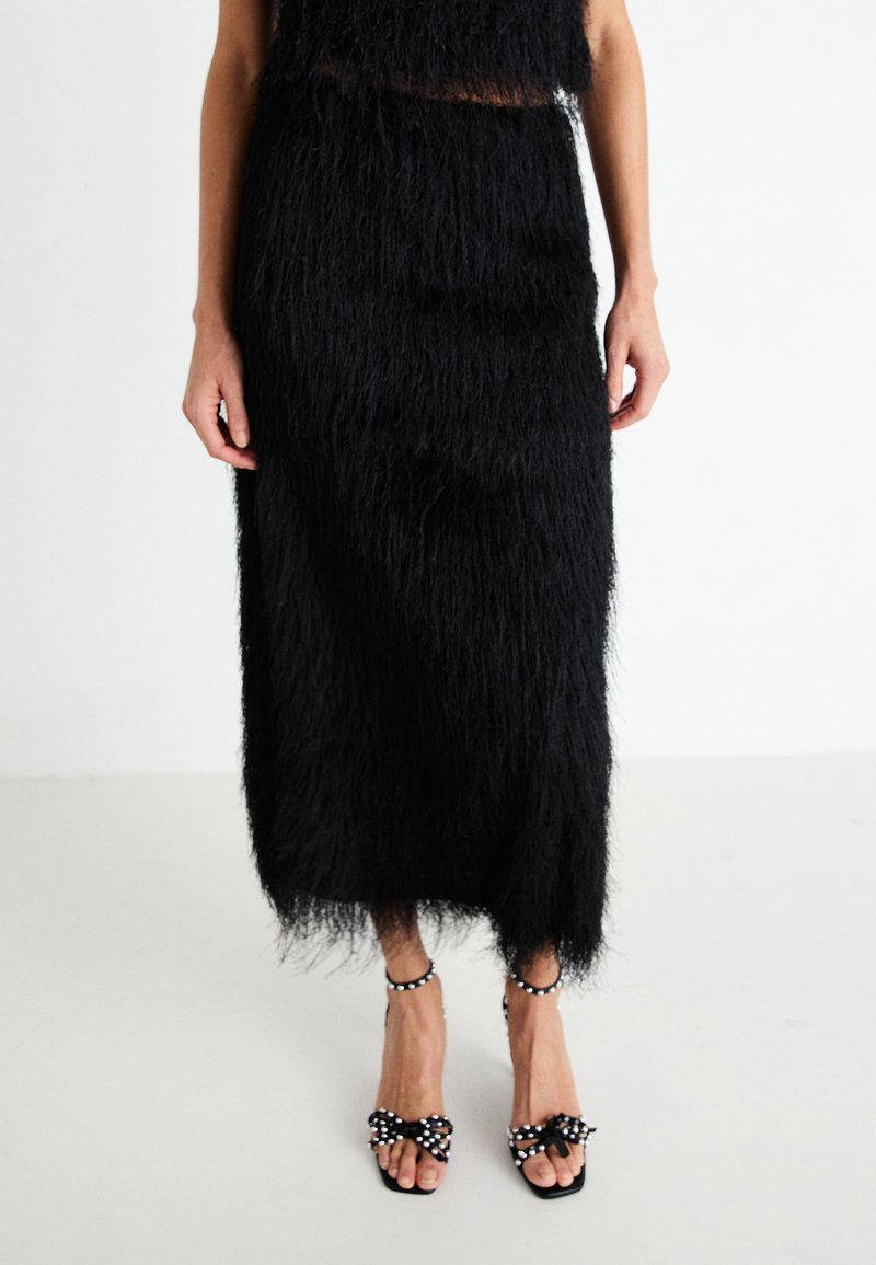 Black fringe two-piece outfit featuring a cropped top and skirt, paired with black sandals adorned with white beads and bows.