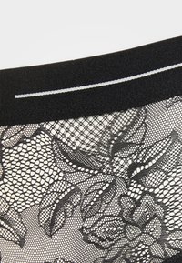 Tissu en dentelle noire avec des motifs floraux et une texture en nid d'abeille, doté d'une ceinture noire lisse et d'une bande contrastante blanche.