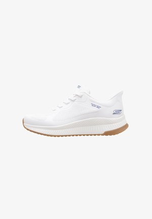 White athletic shoe with mesh panels, textured rubber sole, and a slightly elevated heel. Features lace-up closure and branding on the side.