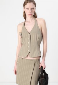 Beige halterneck vest med vertikale hvite striper, med V-utringning, fem knappe-lukking og en tettsittende design, kombinert med et matchende skjørt.