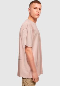 Camiseta de algodón rosa claro con mangas cortas, ajuste relajado y detalle de texto gráfico en el lateral, combinada con pantalones cortos de carga beige.