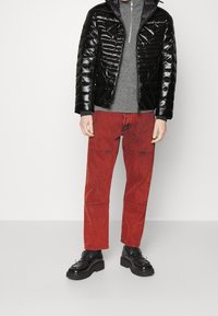 Puffer bunda v lesklé černé, šedý svetr, červené džínové kalhoty s vyšívanými detaily a černé platformové boty se zdobnými akcenty.