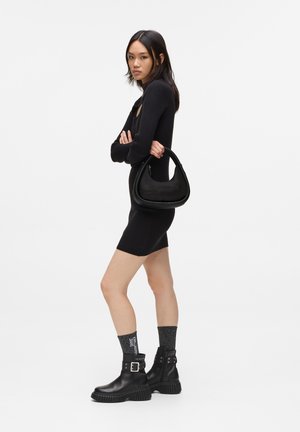 Black leather handbag with a rounded shape and zip closure, worn with a fitted black dress and chunky black boots. Textured gray socks.