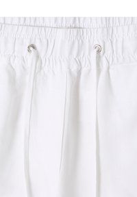 Ceinture élastique blanche avec cordons en tissu passés à travers des œillets métalliques sur un tissu léger.