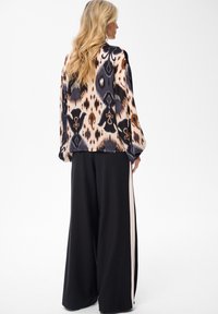 Long-sleeve blouse featuring a multicolored abstract pattern in cream, brown, and black, paired with black wide-leg trousers with beige accents.
