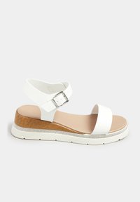 Białe sandały z szerokimi paskami, regulowanym zapięciem, drewnianym koturnem i płaską podstawą, z akcentem w postaci cyrkonii wzdłuż boków.