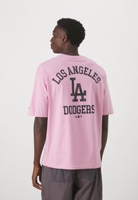 Camiseta de algodón de color rosa claro con cuello redondo, mangas cortas y texto impreso en negro: "LOS ÁNGELES," "LA," y "DODGERS" en la parte posterior.