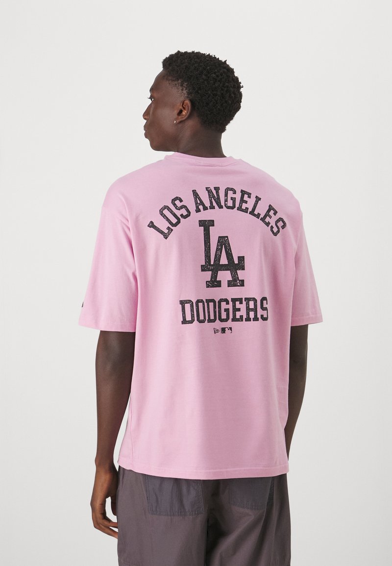 Camiseta de algodón de color rosa claro con cuello redondo, mangas cortas y texto impreso en negro: "LOS ÁNGELES," "LA," y "DODGERS" en la parte posterior.