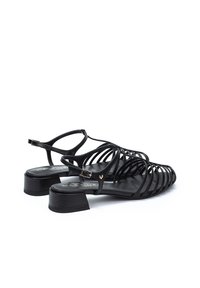Sandalias negras con tiras y tacón bajo, con diseño trenzado, correa para el tobillo ajustable y detalles en tono dorado.