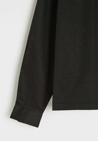 Czarna koszula z długim rękawem, wykonana z gładkiego materiału, pokryta drobnymi srebrnymi akcentami. Manżeta ma schludne, dopasowane wykończenie.