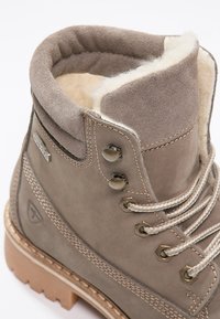Botte d'hiver en cuir marron avec doublure en polaire, œillets métalliques, lacets rayés et semelle en caoutchouc épaisse pour une utilisation en extérieur.