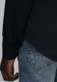 Donker marineblauwe shirt met lange mouwen en knoopmanchetten, met een lichte glans, gecombineerd met lichtblauwe denim jeans met een detail op de achterzak.