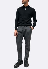 Polo nera a maniche lunghe con colletto a tre bottoni, abbinata a pantaloni grigi affusolati e sneakers nere con lacci. Tessuto liscio e design semplice.