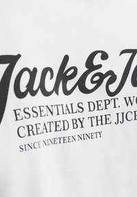 Camiseta de algodón blanca con texto impreso en negro. El diseño incluye el nombre de la marca "Jack & Jones" y detalles adicionales en diferentes tamaños de fuente.