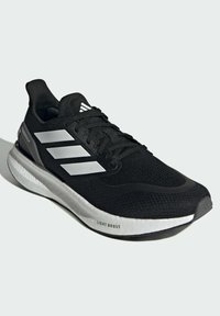 Chaussure de sport noire avec une tige en maille texturée, trois rayures argentées et une semelle blanche rembourrée portant l'inscription "LIGHT BOOST".