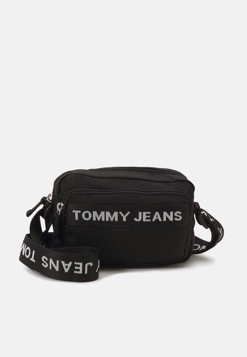 Černá obdélníková crossbody taška s přední kapsou na zip, logo "TOMMY JEANS" na přední straně a nastavitelný ramenní popruh s bílým textem.