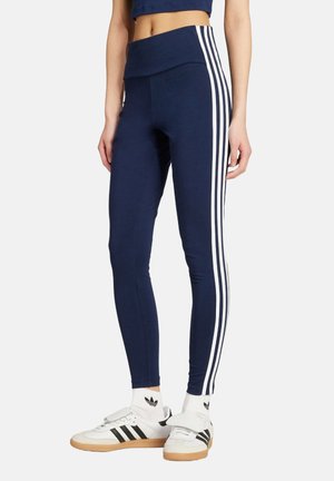 Navy leggings with a wide waistband, featuring three white side stripes. Worn with white sneakers and ribbed ankle socks.