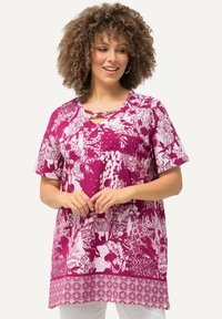 Lila Tunika mit einem auffälligen weißen Blumen- und geometrischen Muster, kurzen Ärmeln und einem V-Ausschnitt mit einem dekorativen Kreuzgurt.
