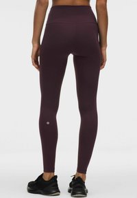 Högmidjade leggings i en djup burgundyröd färg gjorda av elastiskt tyg, med en logoprick vid vristen och en slät yta.