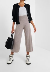 Czarny kardigan, szary top na ramiączkach, beżowe szerokie dzianinowe spodnie, czarna torebka oraz białe sznurowane buty z teksturowaną podeszwą.