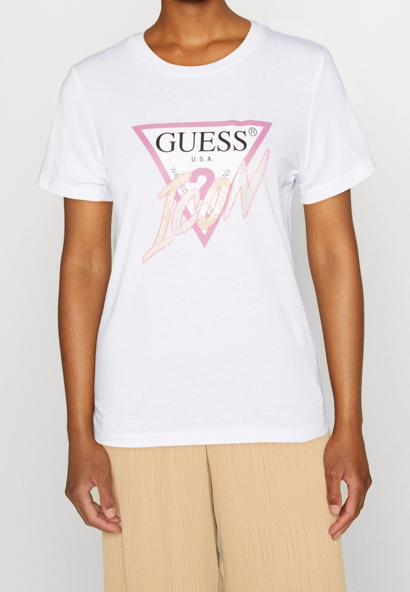 Hvid bomulds t-shirt med et pink trekantet logo, der har "GUESS" og "ICON" i en skinnende skrift. Kortærmet og med rund hals design.