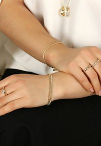 Guld- och silverringar samt armband på händer, med släta ytor och intrikata mönster, kompletterade med ett hängande halsband.