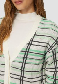 Strickjacke mit V-Ausschnitt, in Cremefarbe mit grünem und schwarzem Streifenmuster und Knopfverschluss. Strukturierter, weicher Stoff.