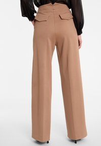 Wijdvallende broek in een lichte tanstof, met een hoge taille, accentueert zakken en een gladde textuur. Aanzicht van achter laat de details duidelijk zien.