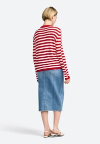 Rot-weiß gestreifter Pullover mit rundem Ausschnitt, kombiniert mit einem hellblauen Denim-Midirock. Das Outfit wird von flachen, beigen Schuhen ergänzt.