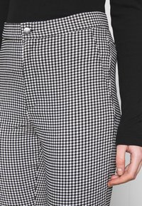 Kalhoty s vzorem houndstooth v černobílé barvě s přiléhavým střihem, které mají stříbrný knoflík a boční kapsy.