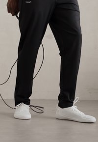 Sorte treningsbukser med en glatt tekstur og slim fit, kombinert med hvite joggesko med perforerte detaljer og flate snører.