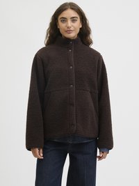 Pruun fliisjakker kõrge kraega, nupud ja suured taskud. Omab pehmet, tekstureeritud pinna ja lõdva lõikega.