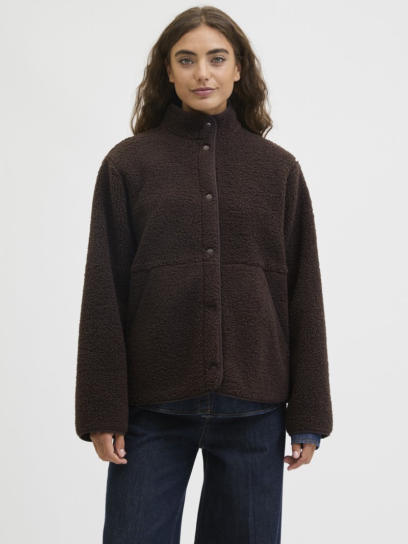 Pruun fliisjakker kõrge kraega, nupud ja suured taskud. Omab pehmet, tekstureeritud pinna ja lõdva lõikega.