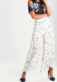 Top negro con estampado floral y hombros al aire, combinado con pantalones anchos color crema con un estampado floral azul. Unos zapatos en color marino completan el conjunto.