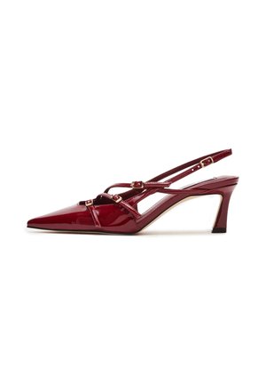 Décolleté a punta in vernice rossa con cinturini alla caviglia e un design a tacco medio stretto. Presentano dettagli con fibbie in metallo.