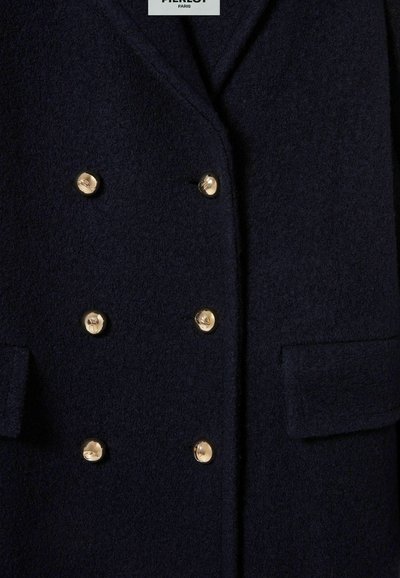 Cappotto di lana blu navy con design doppiopetto caratterizzato da bottoni dorati, due tasche frontali e una consistenza morbida. Etichetta del marchio visibile nella parte alta.