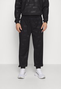 Černý teplákový komplet s jemným reliéfním vzorem loga "ADIDAS", elastickým pasem a manžetami. Spárováno s bílými sportovními botami.