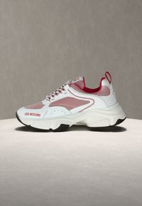 Λευκό και κόκκινο αθλητικό παπούτσι Love Moschino με διχτυωτά πάνελ, παχύ πέλμα και λογότυπο στην πλευρά, εμφανιζόμενο σε φωτεινή επιφάνεια με γκρι φόντο.