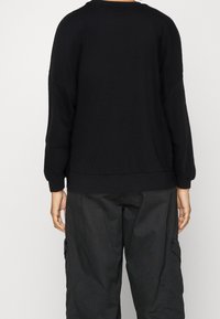 Sudadera negra de gran tamaño con escote redondo y hombros caídos. Presenta puños y dobladillo acanalados, hecha de una suave tela texturada.