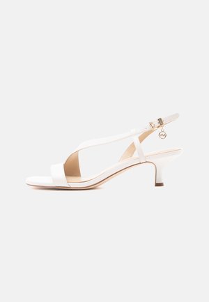 Witte sandaal met open teen, lage hak, slingback bandje, gouden gesp en een kleine ronde bedelhanger.