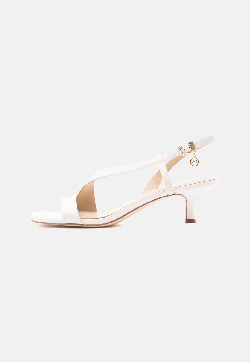 Λευκό σανδάλι με ανοιχτά δάχτυλα, χαμηλό τακούνι, λουράκι πίσω από τη φτέρνα, χρυσή αγκράφα και μικρό στρογγυλό μενταγιόν.