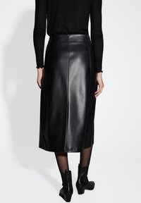 Jupe midi en cuir noir avec une texture lisse, présentant une taille haute et des détails de couture subtils, associée à des bottines noires.